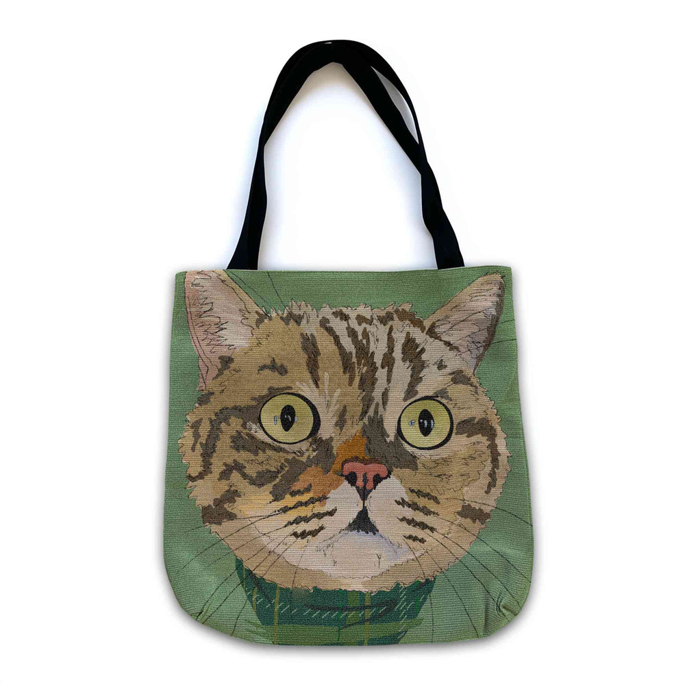 A woven tote bag with black shoulder straps featuring a custom illustrated cat portrait of a tabby cat wearing a plaid bandana set against a subtle textured green background printed on the side of the bag, shown on a clean white background.