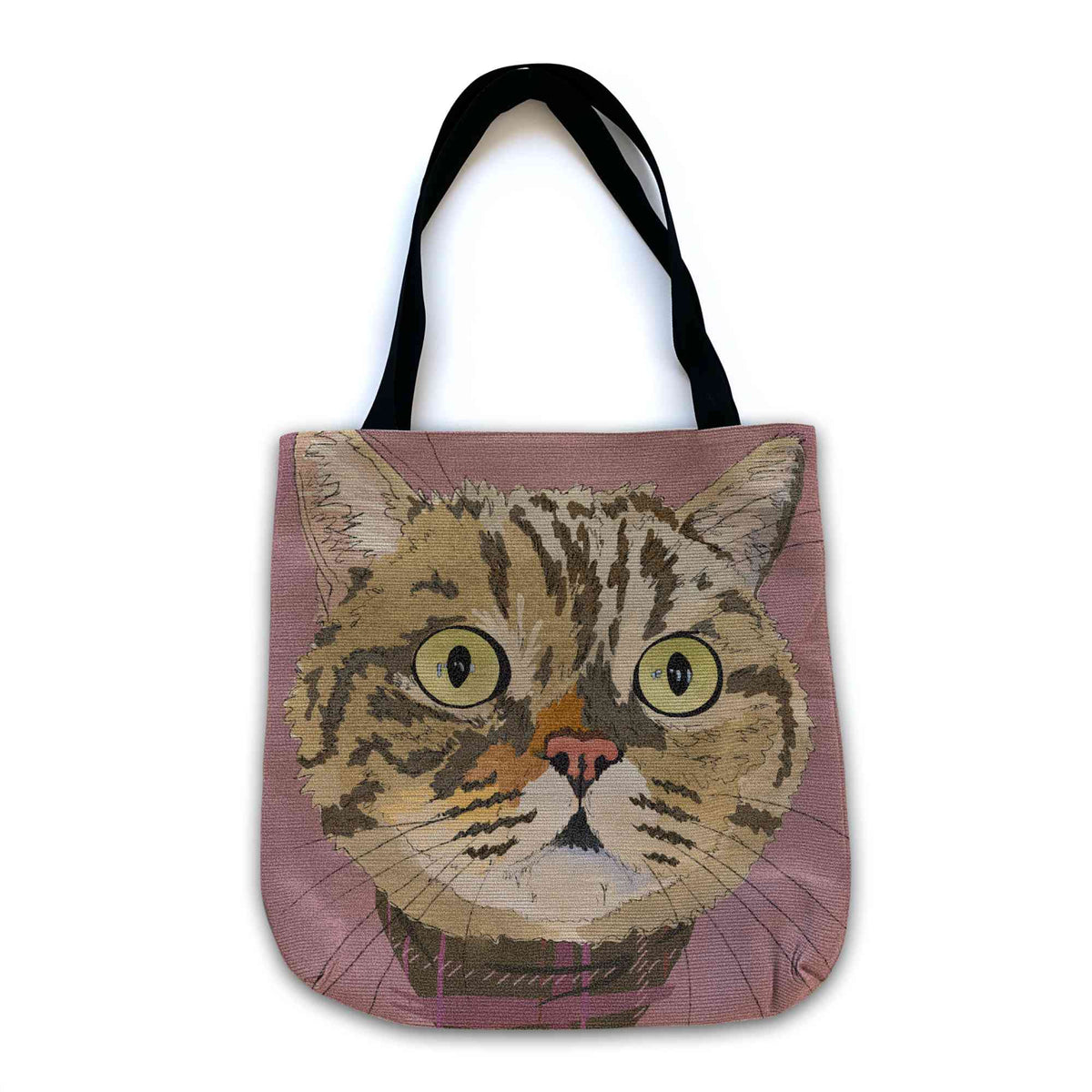A woven tote bag with black shoulder straps featuring a custom illustrated cat portrait of a tabby cat wearing a plaid bandana set against a subtle textured dusty rose background printed on the side of the bag, shown on a clean white background. 
