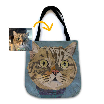 A woven tote bag with black shoulder straps featuring a custom illustrated cat portrait of a tabby cat wearing a plaid bandana set against a subtle textured blue background printed on the side of the bag, shown on a clean white background. A small inset photo of the cat appears in the upper left with a yellow arrow pointing to the bag design, indicating the custom design was drawn from the photo.