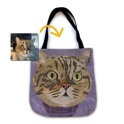 A woven tote bag with black shoulder straps featuring a custom illustrated cat portrait of a tabby cat wearing a plaid bandana set against a subtle textured lavender background printed on the side of the bag, shown on a clean white background. A small inset photo of the cat appears in the upper left with a yellow arrow pointing to the bag design, indicating the custom design was drawn from the photo.