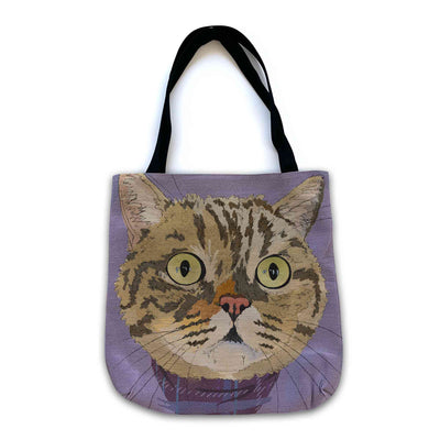 A woven tote bag with black shoulder straps featuring a custom illustrated cat portrait of a tabby cat wearing a plaid bandana set against a subtle textured lavender background printed on the side of the bag, shown on a clean white background. 