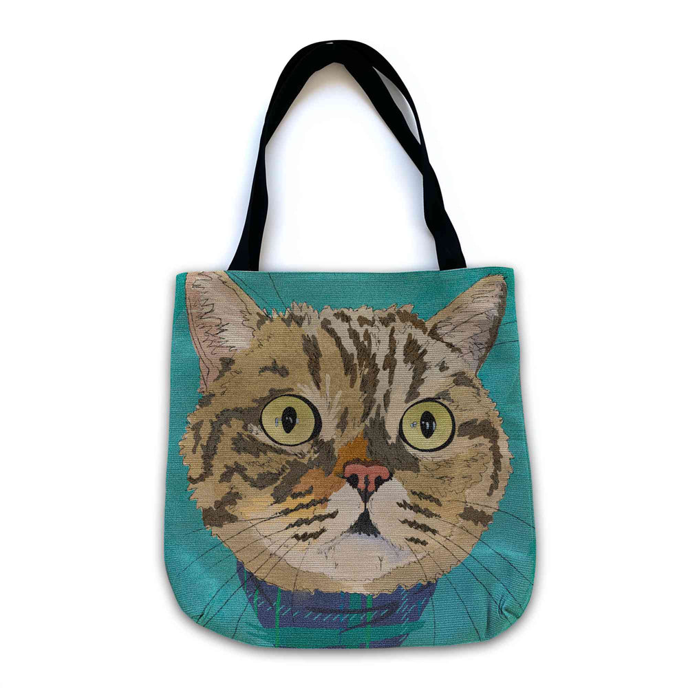 A woven tote bag with black shoulder straps featuring a custom illustrated cat portrait of a tabby cat wearing a plaid bandana set against a subtle textured teal background printed on the side of the bag, shown on a clean white background. 