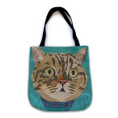 A woven tote bag with black shoulder straps featuring a custom illustrated cat portrait of a tabby cat wearing a plaid bandana set against a subtle textured teal background printed on the side of the bag, shown on a clean white background. 