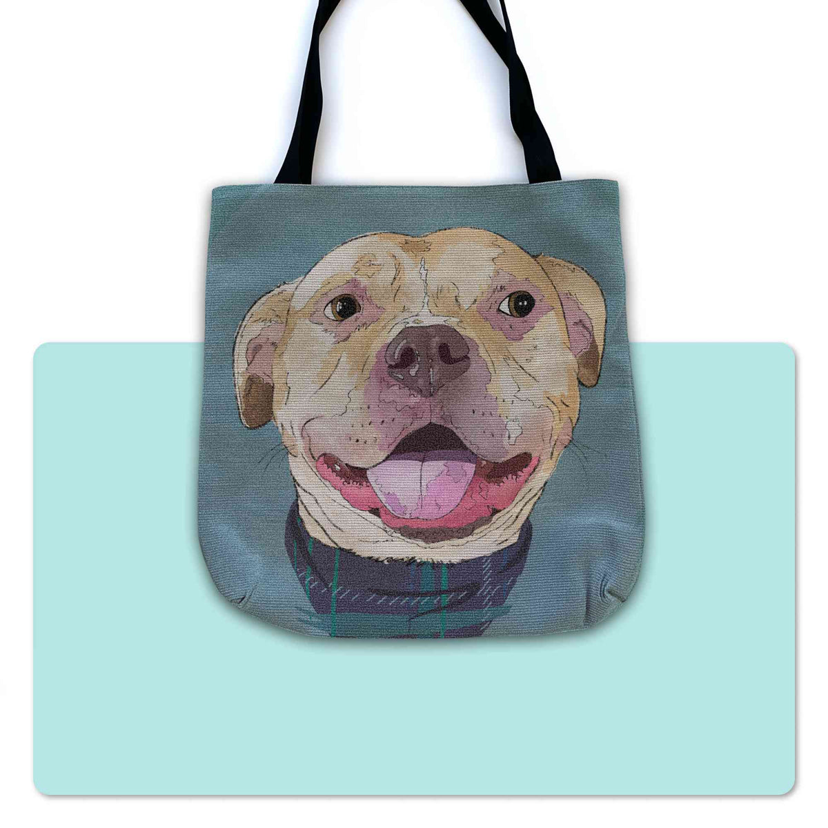 A woven tote bag with black shoulder straps featuring a custom illustrated dog portrait of a smiling tan dog wearing a plaid bandana set against a subtle textured blue background printed on the side of the bag, shown centered over a large light aqua rectangular shape on a white background.