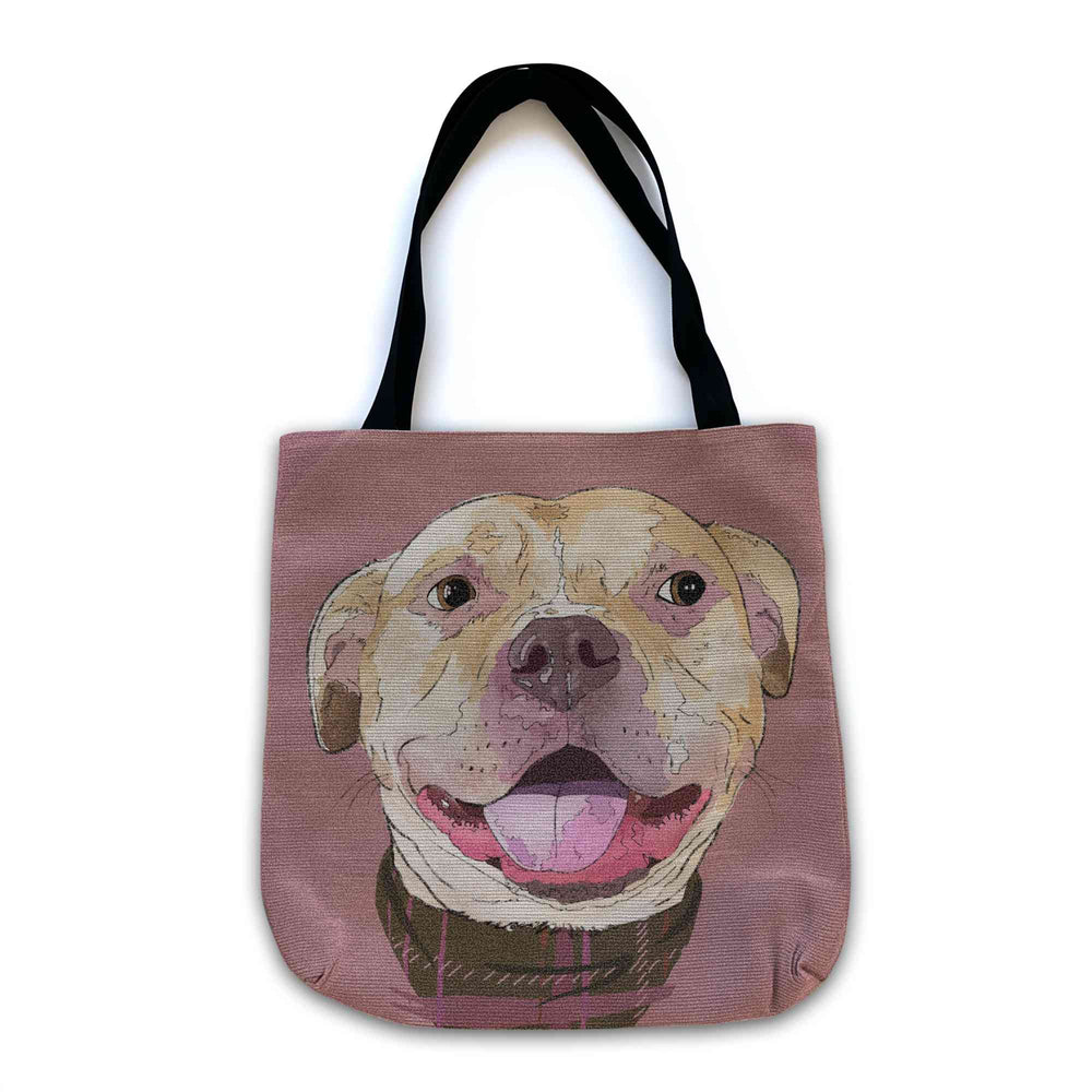 A woven tote bag with black shoulder straps featuring a custom illustrated dog portrait of a smiling tan dog wearing a plaid bandana set against a subtle textured dusty rose background printed on the side of the bag, shown on a clean white background.
