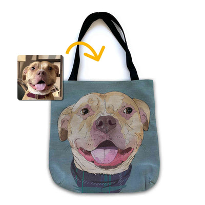 A woven tote bag with black shoulder straps featuring a custom illustrated dog portrait of a smiling tan dog wearing a plaid bandana set against a subtle textured blue background printed on the side of the bag, shown on a clean white background. A small inset photo of the dog appears in the upper left with a yellow arrow pointing to the bag design, indicating the custom design was drawn from the photo.