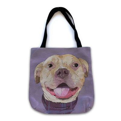 A woven tote bag with black shoulder straps featuring a custom illustrated dog portrait of a smiling tan dog wearing a plaid bandana set against a subtle textured lavender background printed on the side of the bag, shown on a clean white background. 