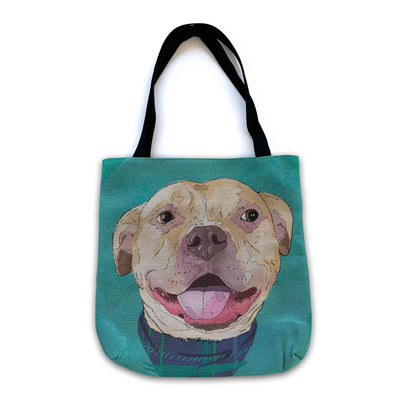 A woven tote bag with black shoulder straps featuring a custom illustrated dog portrait of a smiling tan dog wearing a plaid bandana set against a subtle textured teal background printed on the side of the bag, shown on a clean white background. 