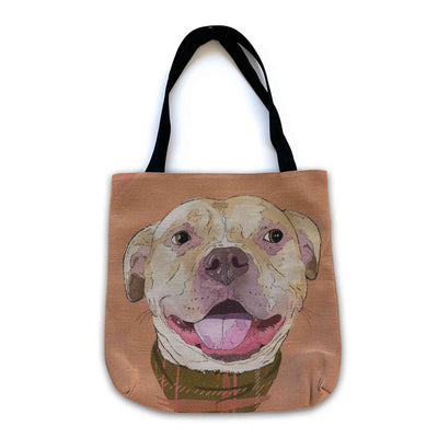 A woven tote bag with black shoulder straps featuring a custom illustrated dog portrait of a smiling tan dog wearing a plaid bandana set against a subtle textured orange background printed on the side of the bag, shown on a clean white background.