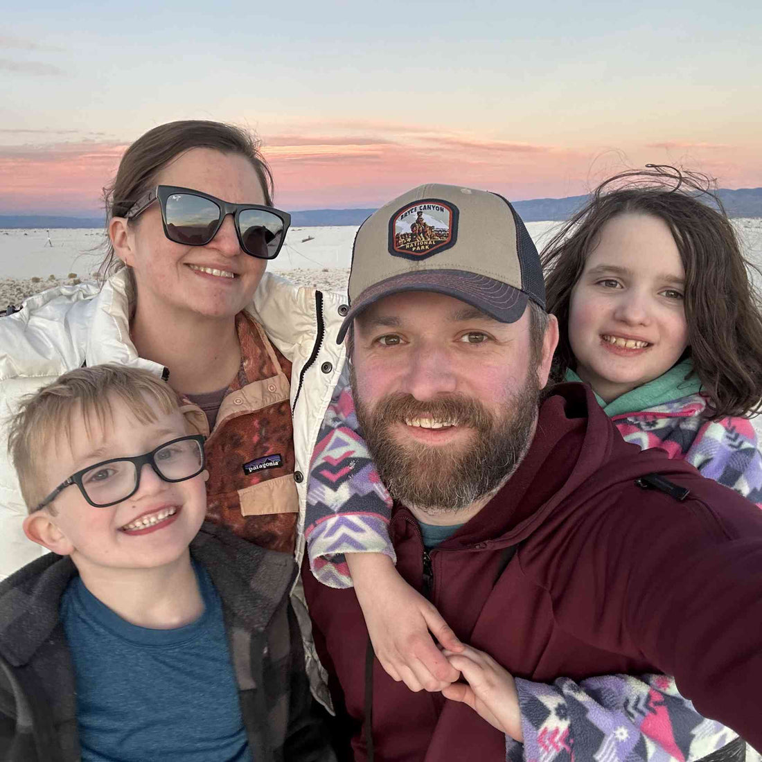 A family taking a selfie outdoors at sand dunes at sunset.
